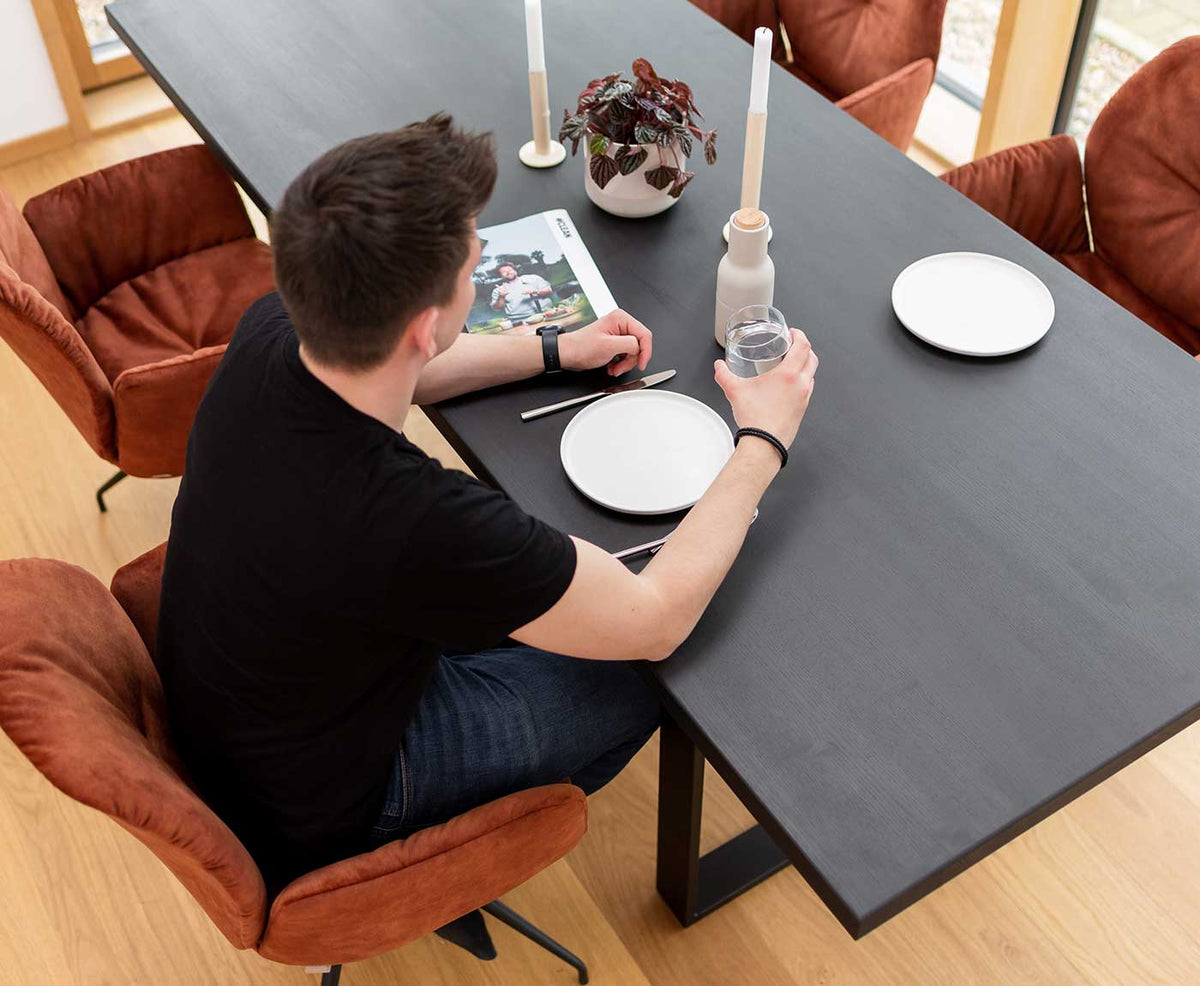 Tischplatte Schwarz mit Gestell sowie Stühlen und Person am Trinken