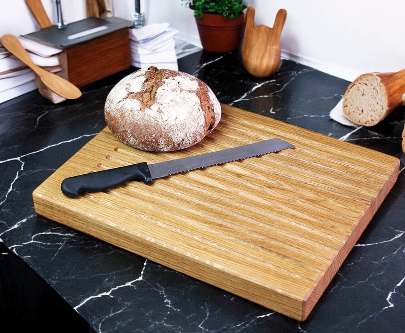 Brotschneidebrett aus Eiche mit Rillen, Brotlaib und Messer als Dekoration.