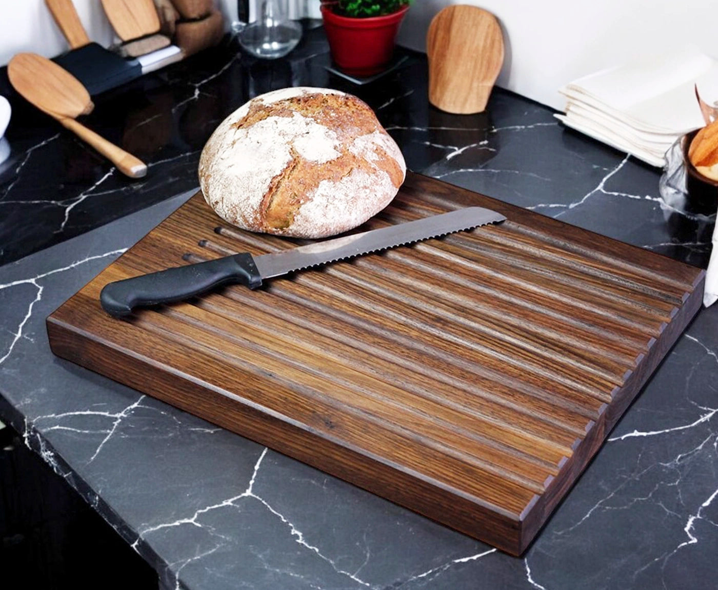 Brotschneidebrett mit Rillen, Brotlaib und Messer auf Küchenarbeitsplatte.