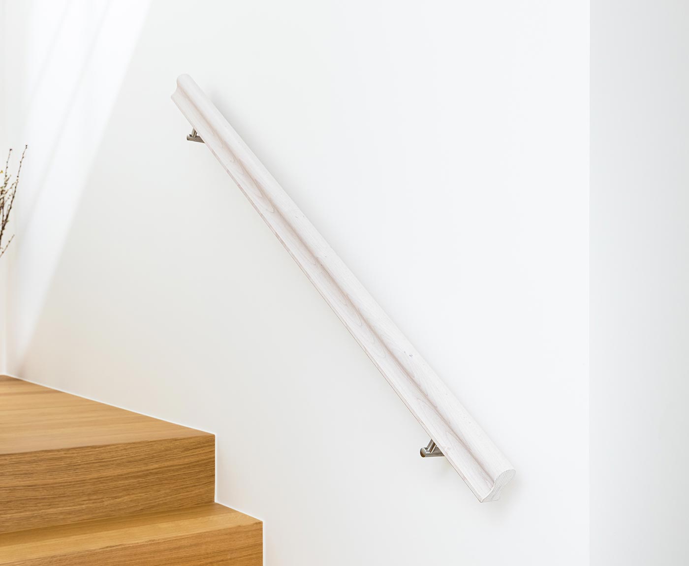 Weißer Handlauf Holz in Omega als Treppengeländer innen über Holztreppe an weiße Wand montiert.
