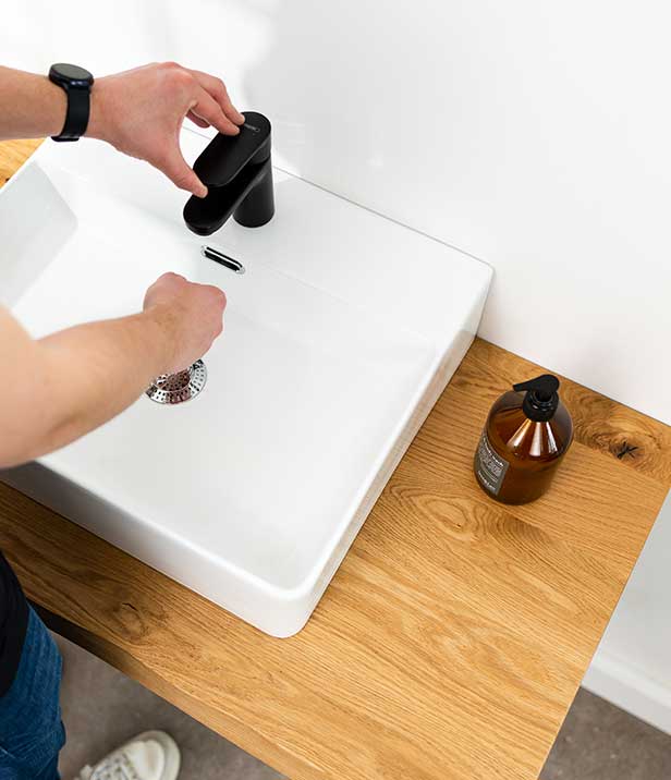 Junger Mann steht an der Waschtischplatte und wäscht sich die Hände